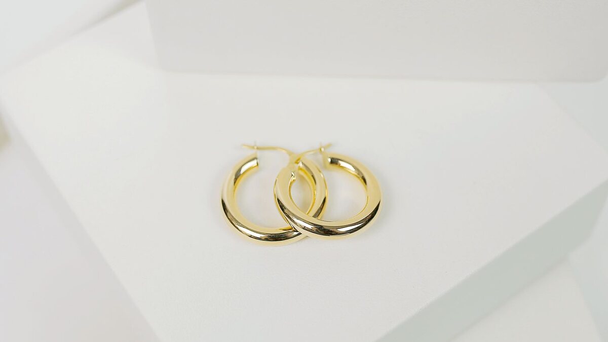 Paire de boucles d'oreilles pendantes créoles dorées posées sur un fond neutre