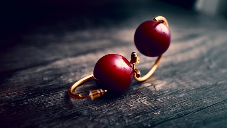 Boucles d'oreilles à perle rouge sombre posées sur un plateau de bois